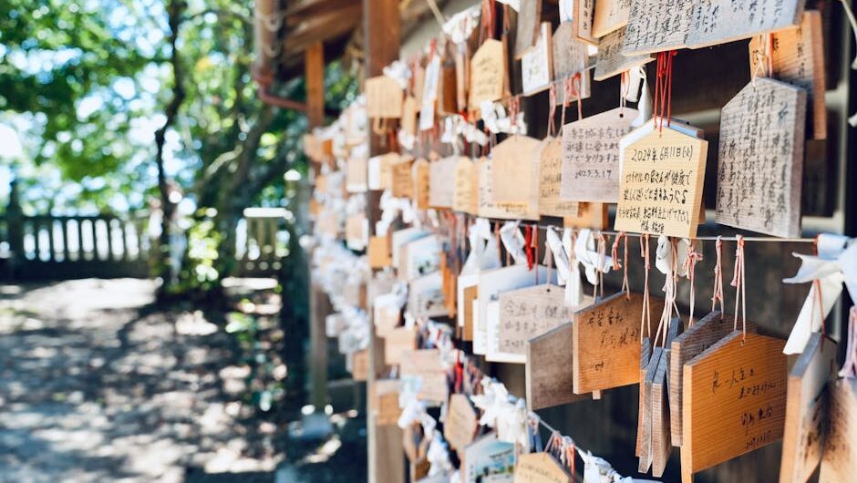 A serene scene of wooden ema plaques hanging at a Japanese temple, surrounded by lush greenery.