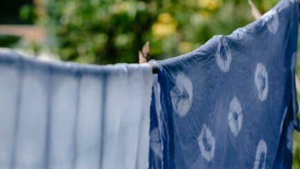 Shibori-dyed indigo fabrics drying in a serene outdoor setting with lush greenery.